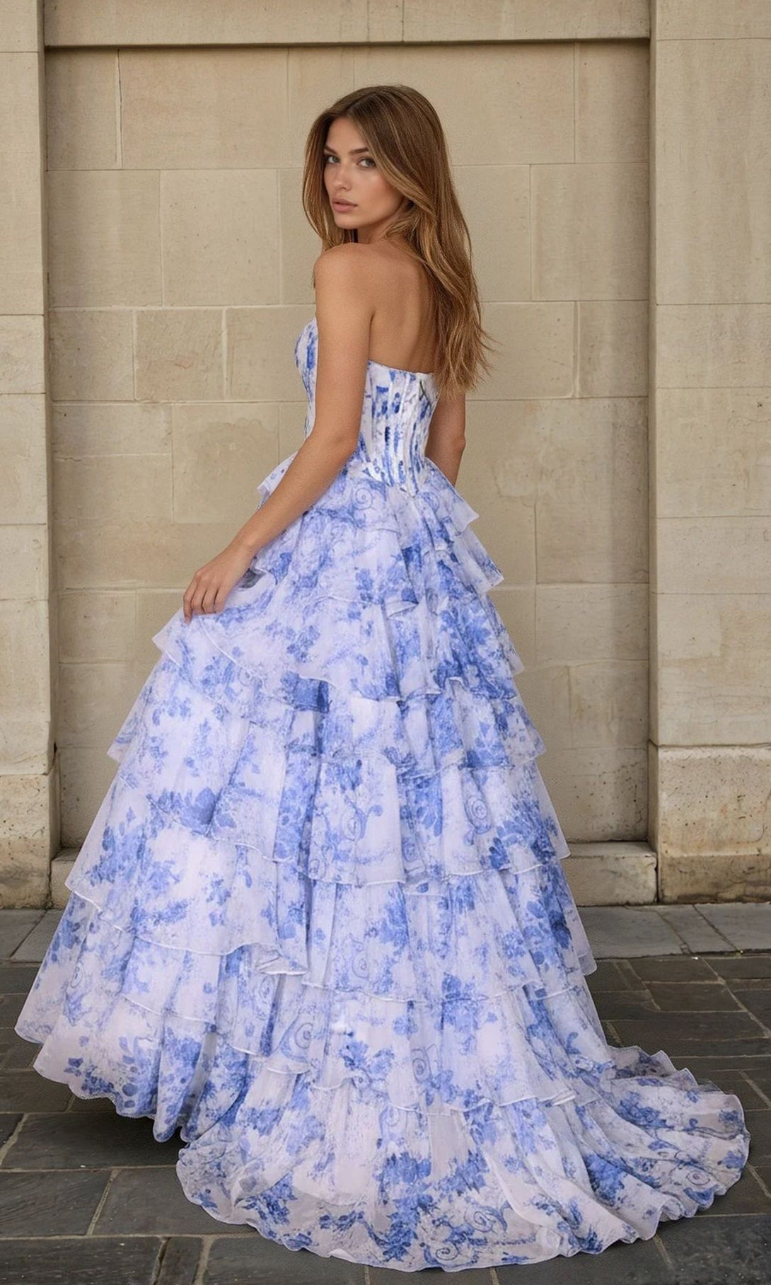 Woman in a blue floral dress standing against a stone wall.